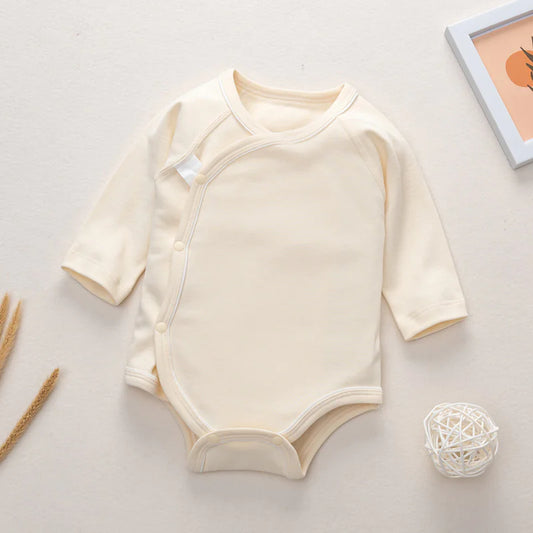 A beige long-sleeve newborn romper with open buttons at the bottom, displayed on a neutral background with decorative items around it.