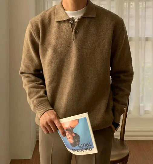 A man sitting at a table wearing a black long-sleeved polo collar buttoned sweater, with a white cup on the table.