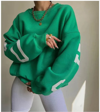 A woman wearing a beige sweatshirt with green printed text on the sleeves.