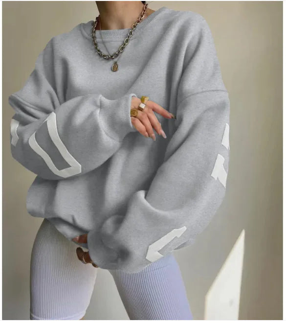 A woman wearing a beige sweatshirt with green printed text on the sleeves.