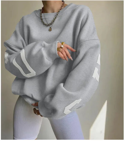 A woman wearing a beige sweatshirt with green printed text on the sleeves.