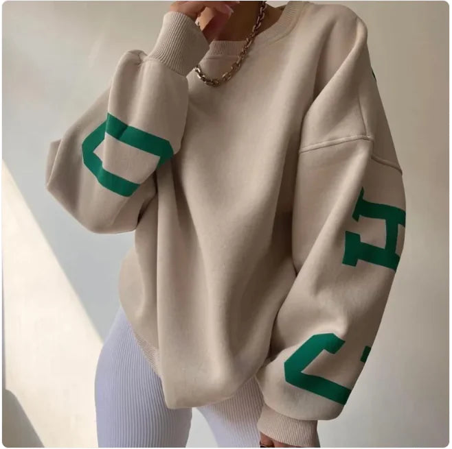 A woman wearing a beige sweatshirt with green printed text on the sleeves.