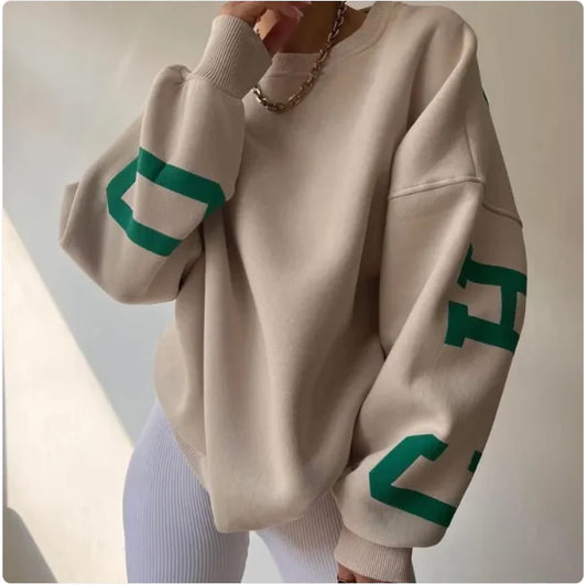 A woman wearing a beige sweatshirt with green printed text on the sleeves.