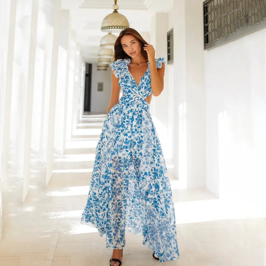 A woman wearing a blue floral v-neck ruffle dress with long sleeves, standing in a white hallway with columns.