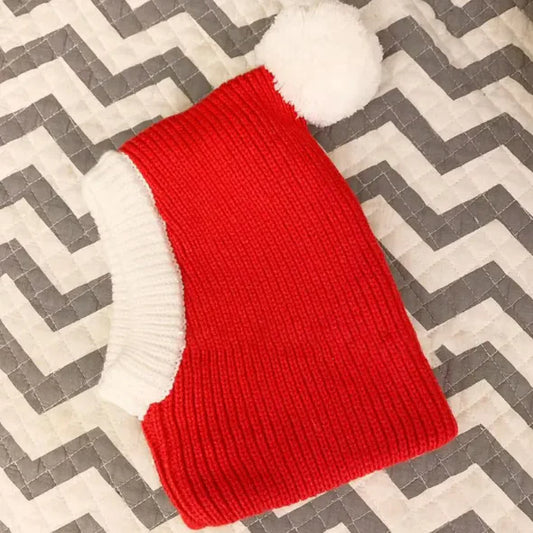 A red and white striped woolen pet hat with a white pom-pom on a grey background.